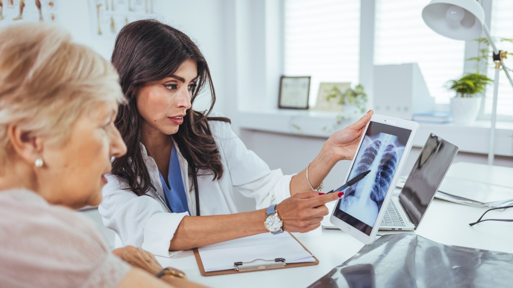 Doctor explaining lung x-ray results on a tablet to an elderly patient with a smoking problem in the medical clinic